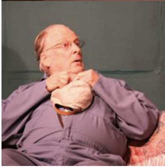 An elderly woman with glasses and short blonde hair, sitting on a couch, holding a beige cat.