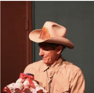 Woman wearing a cowboy hat and beige shirt holding a gift wrapped with red and white paper.