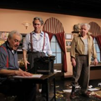 Three men in a room with a black piano, some papers on the floor, and curtains on the windows, engaged in a conversation or performance.