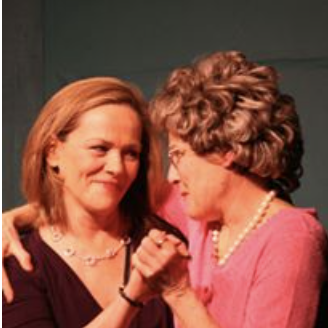 Two women, one with red hair and the other with curly brown hair, holding hands and smiling at each other.