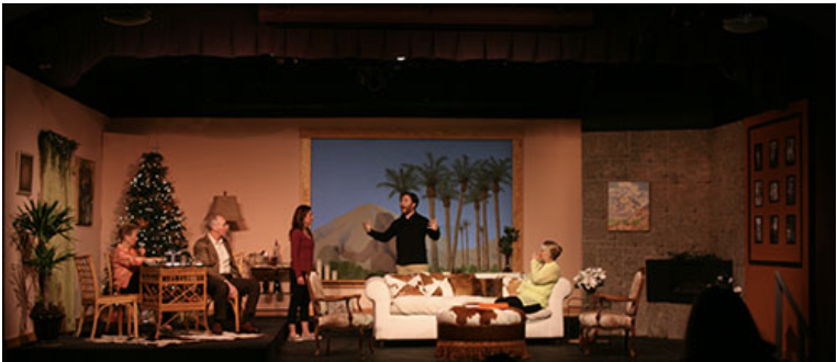 A theater stage set depicting an interior room with five actors, decorated with plants, a Christmas tree, and landscape backdrop with mountains and trees.