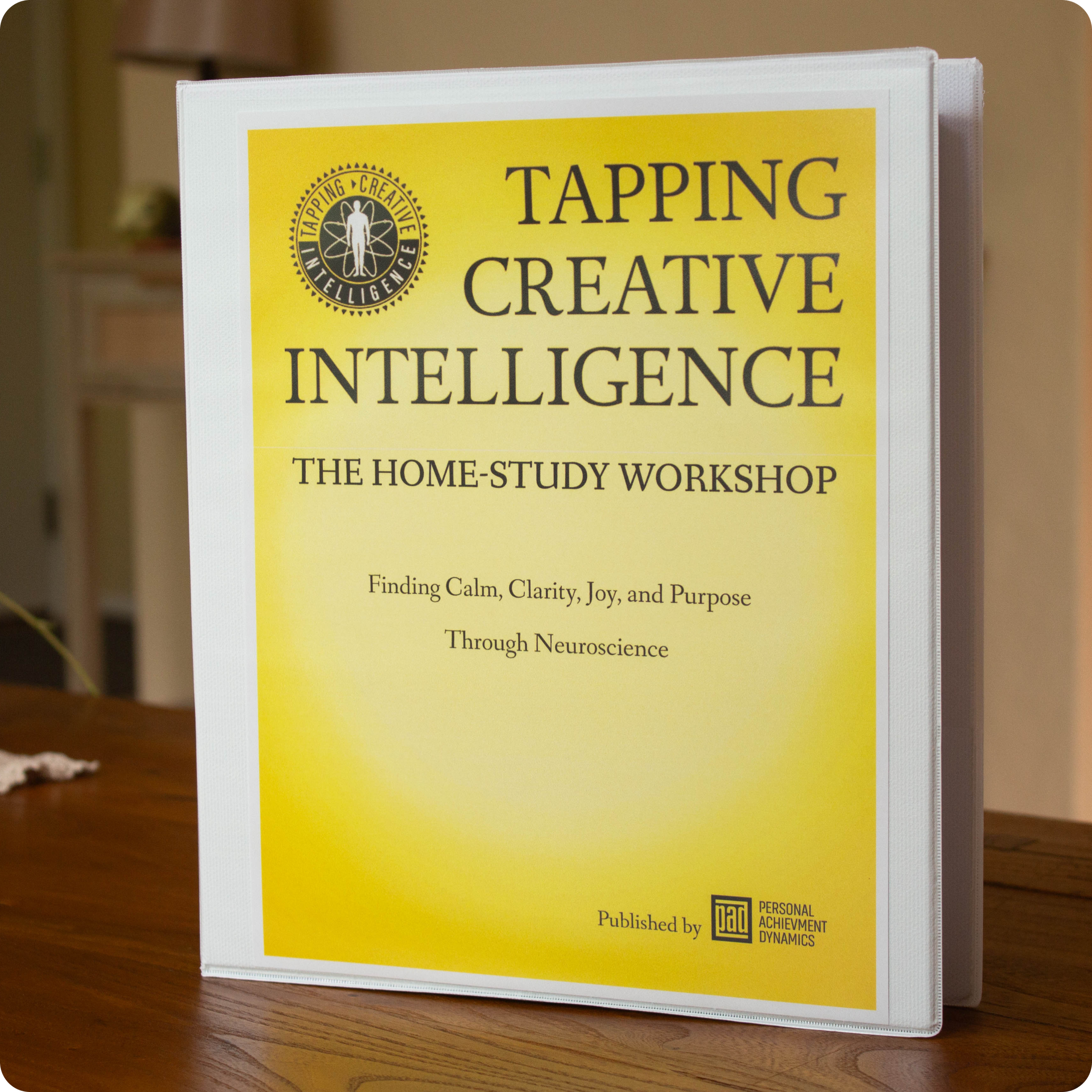 A yellow and white book cover titled "Tapping Creative Intelligence" with a logo on the top left corner and text indicating it is a home-study workshop, published by the Personal Achievement Dynamics organization.