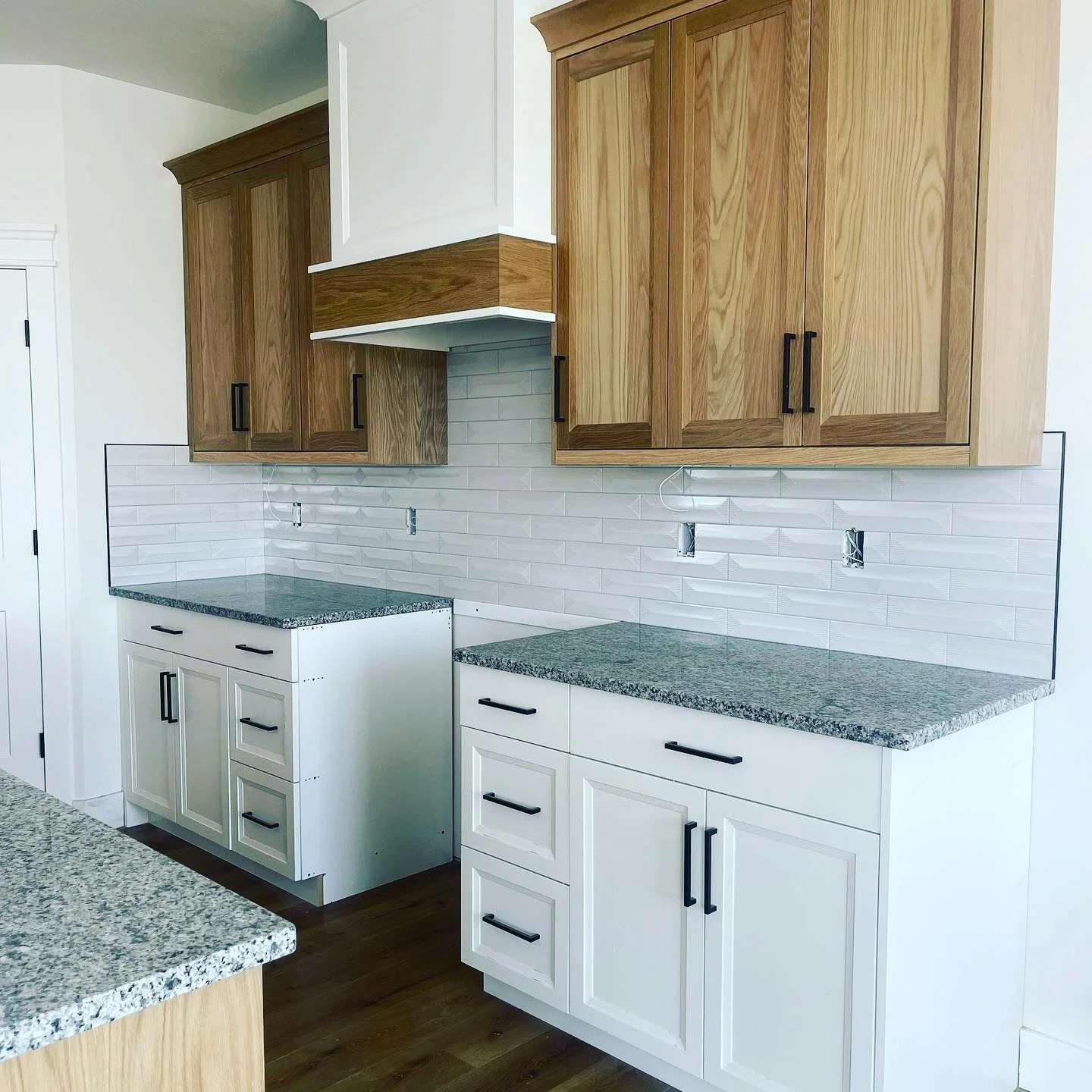 Kitchen with white and wooden cabinets, granite countertops, white subway tile backsplash, and empty wall outlets.