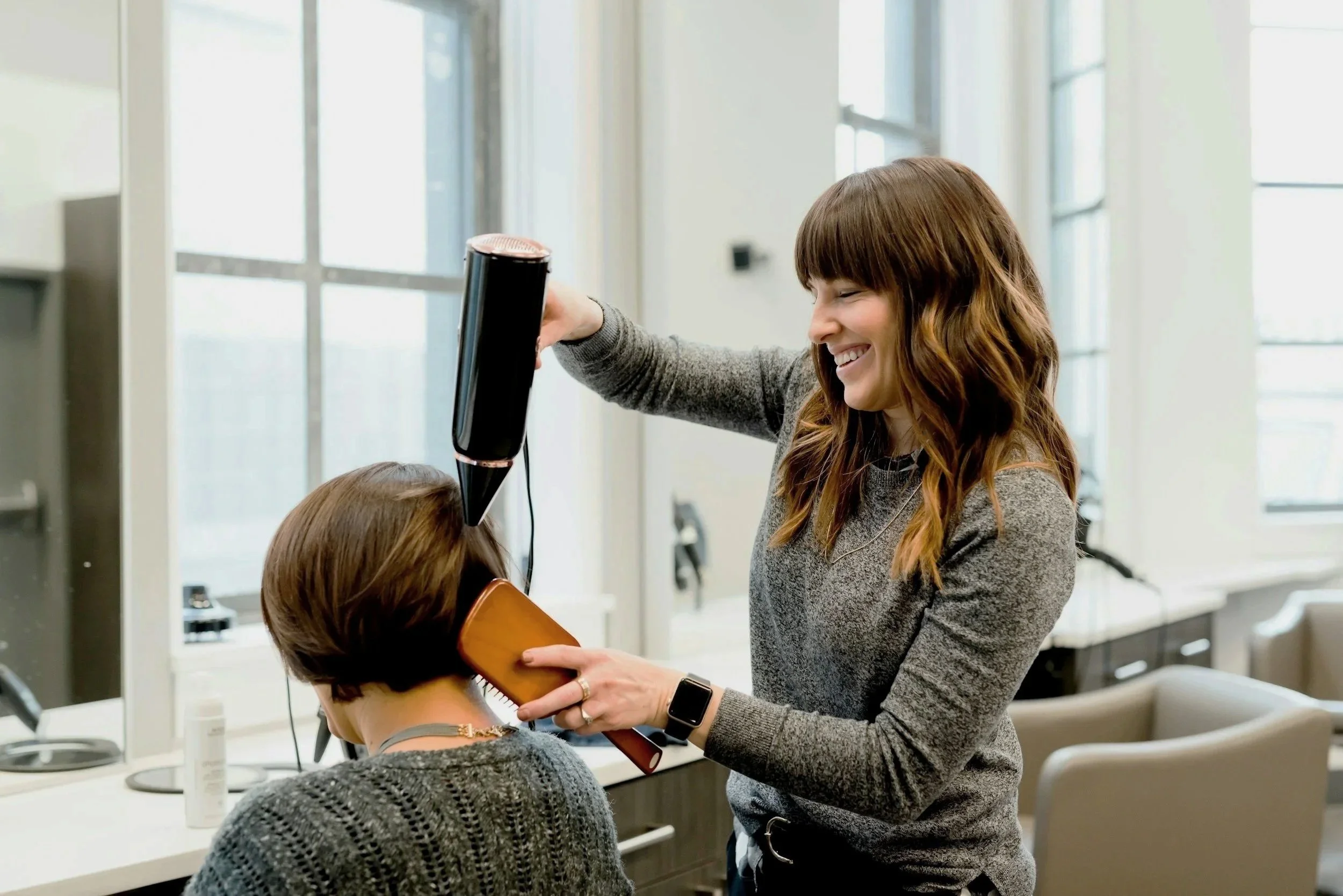 A hairstylist blow drying a client's hair in a salon.