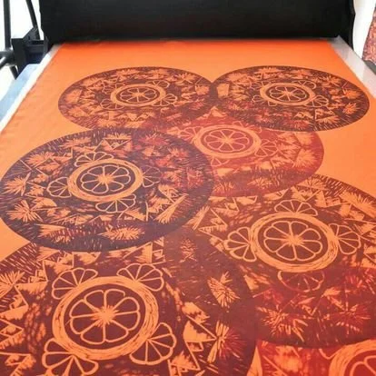 Estampado en tela de color naranja con círculos negros decorados con flores y patrones tropicales.