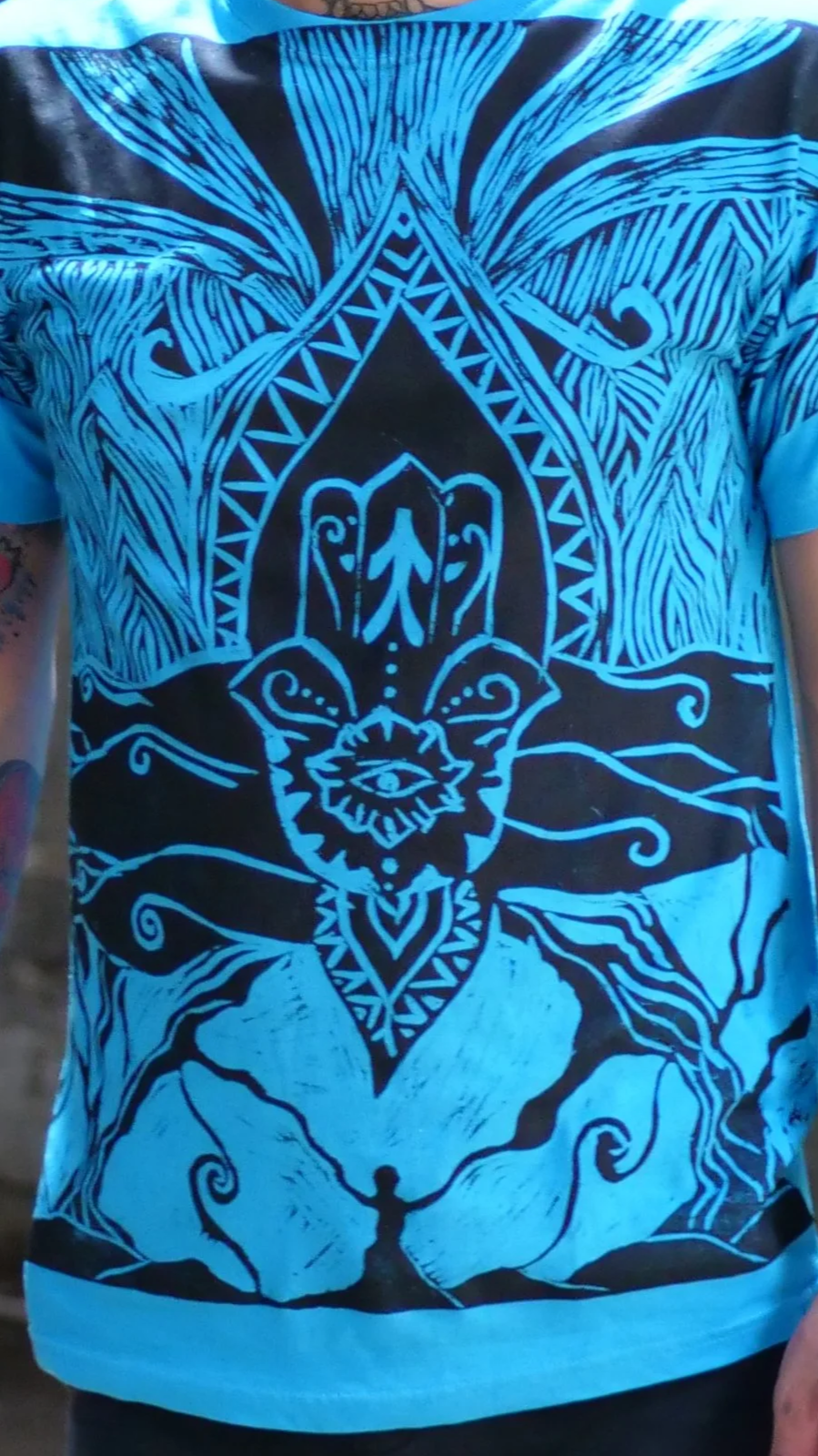 Diseño artístico en colores azules y negros que muestra una figura central con un ojo en el centro, rodeada de formas y patrones abstractos, con una figura humana en la parte inferior sosteniendo una rama o serpiente.