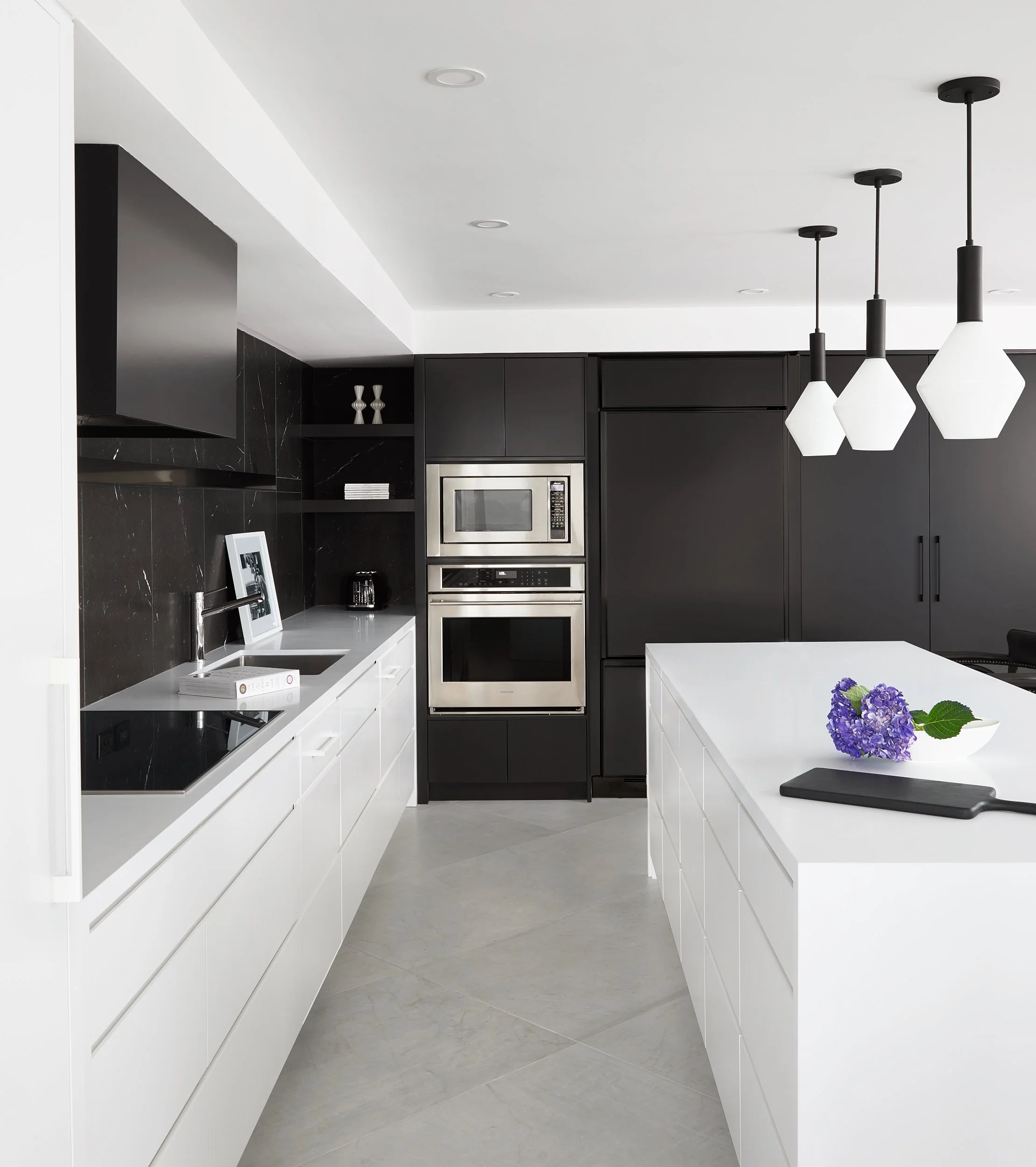 Modern kitchen with white and black cabinets, stainless steel appliances, a white island with purple flowers, and black and white pendant lights.