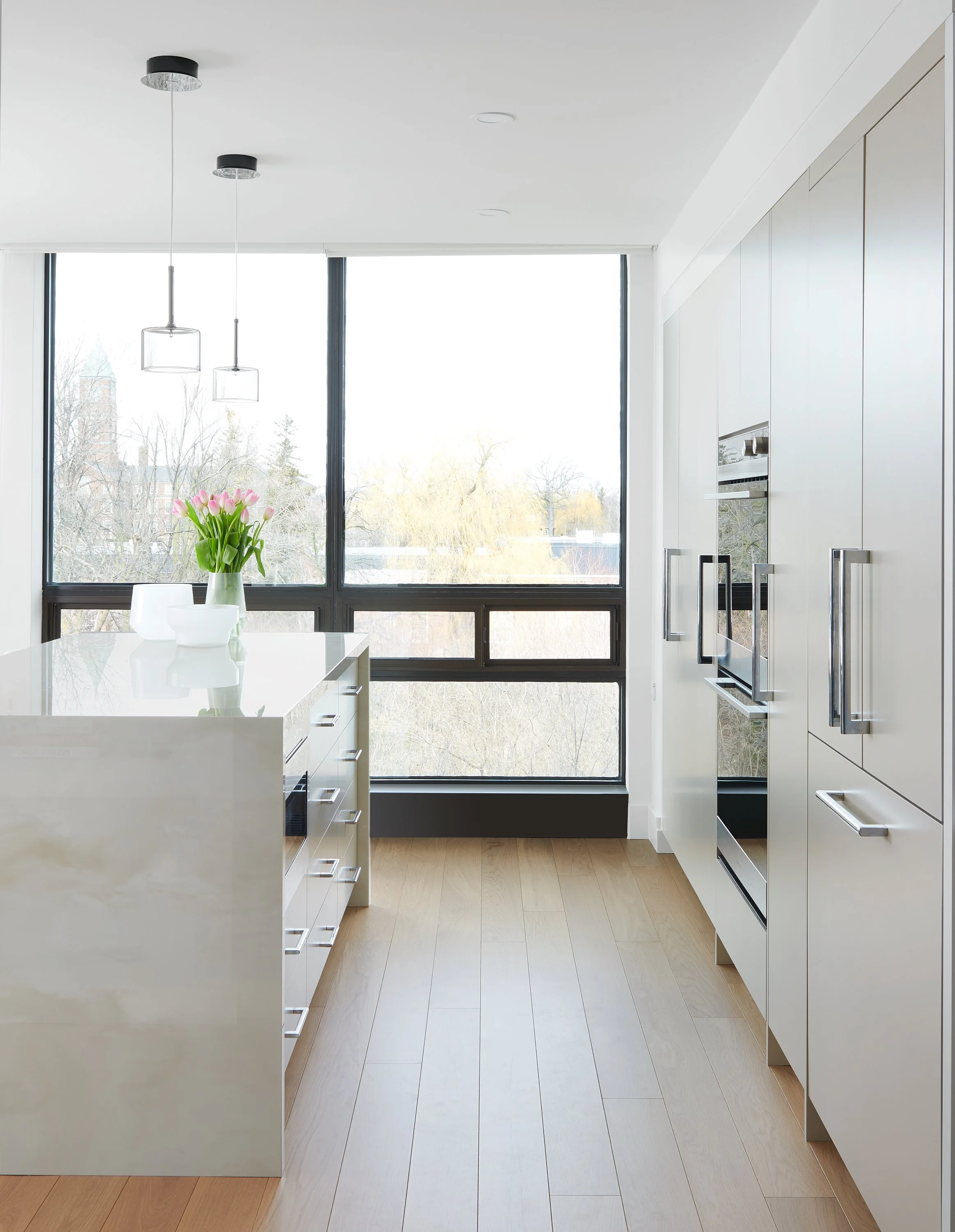 Modern kitchen with white cabinetry, a large window, a kitchen island with a vase of pink tulips, and built-in appliances.
