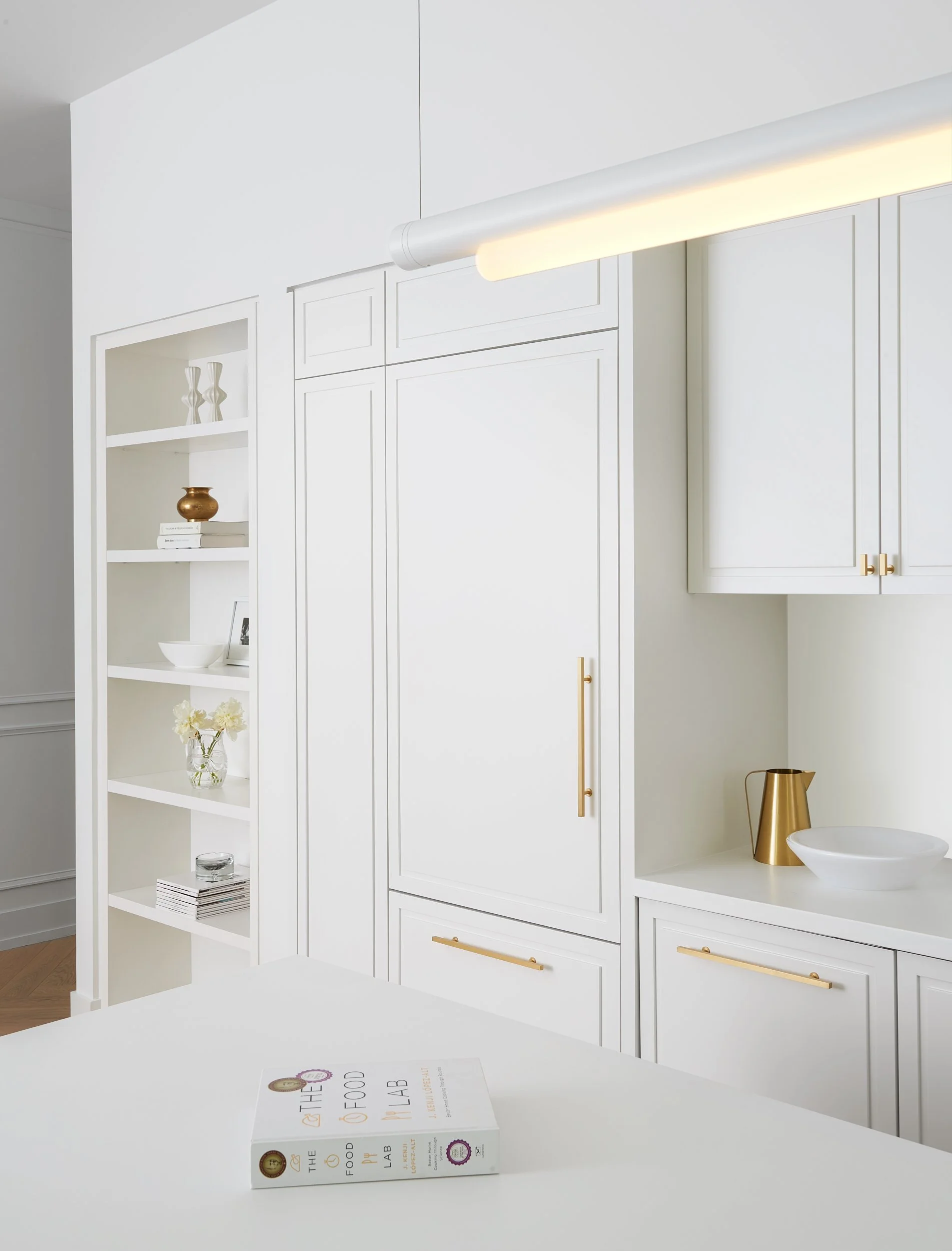 Modern white kitchen with gold accents, a book on the countertop, and built-in cabinets.