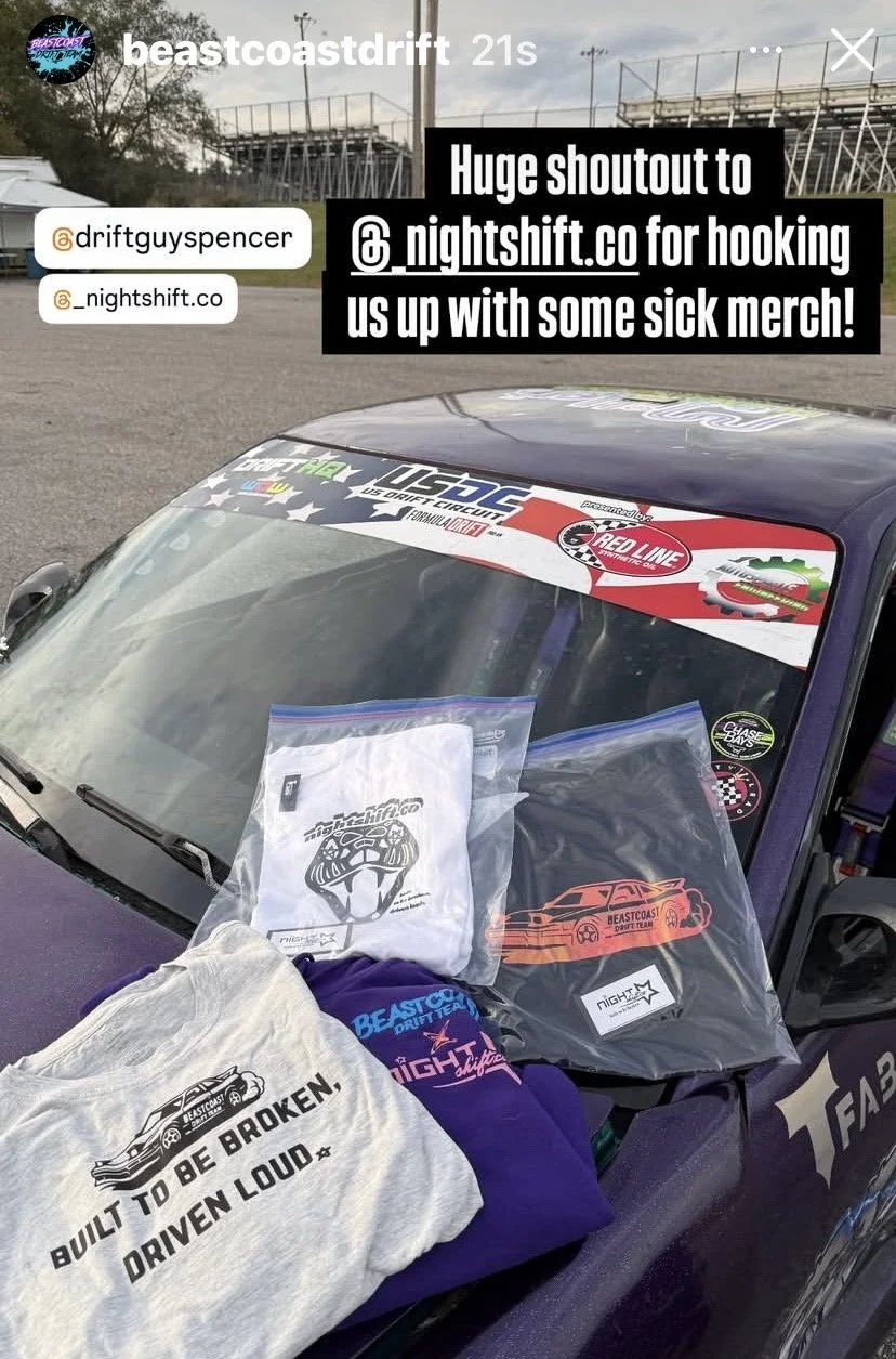 Car with racing decals, merchandise including shirts and hats on the hood, at a race track. Text overlay giving shoutout to Nightshift.co for merchandise.