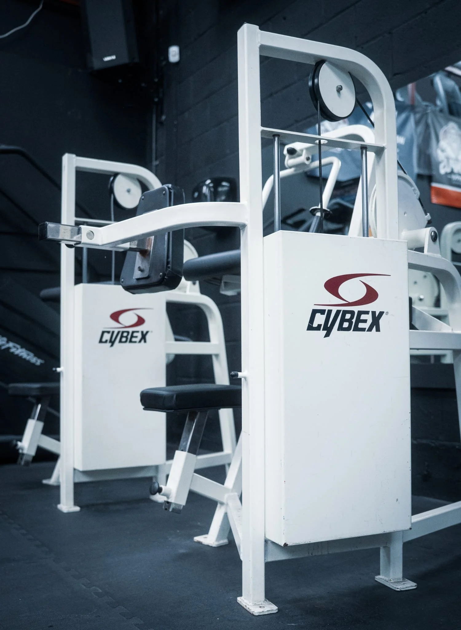 Cybex workout equipment in gym, including a seated chest press machine, with black and white interior and dark flooring.