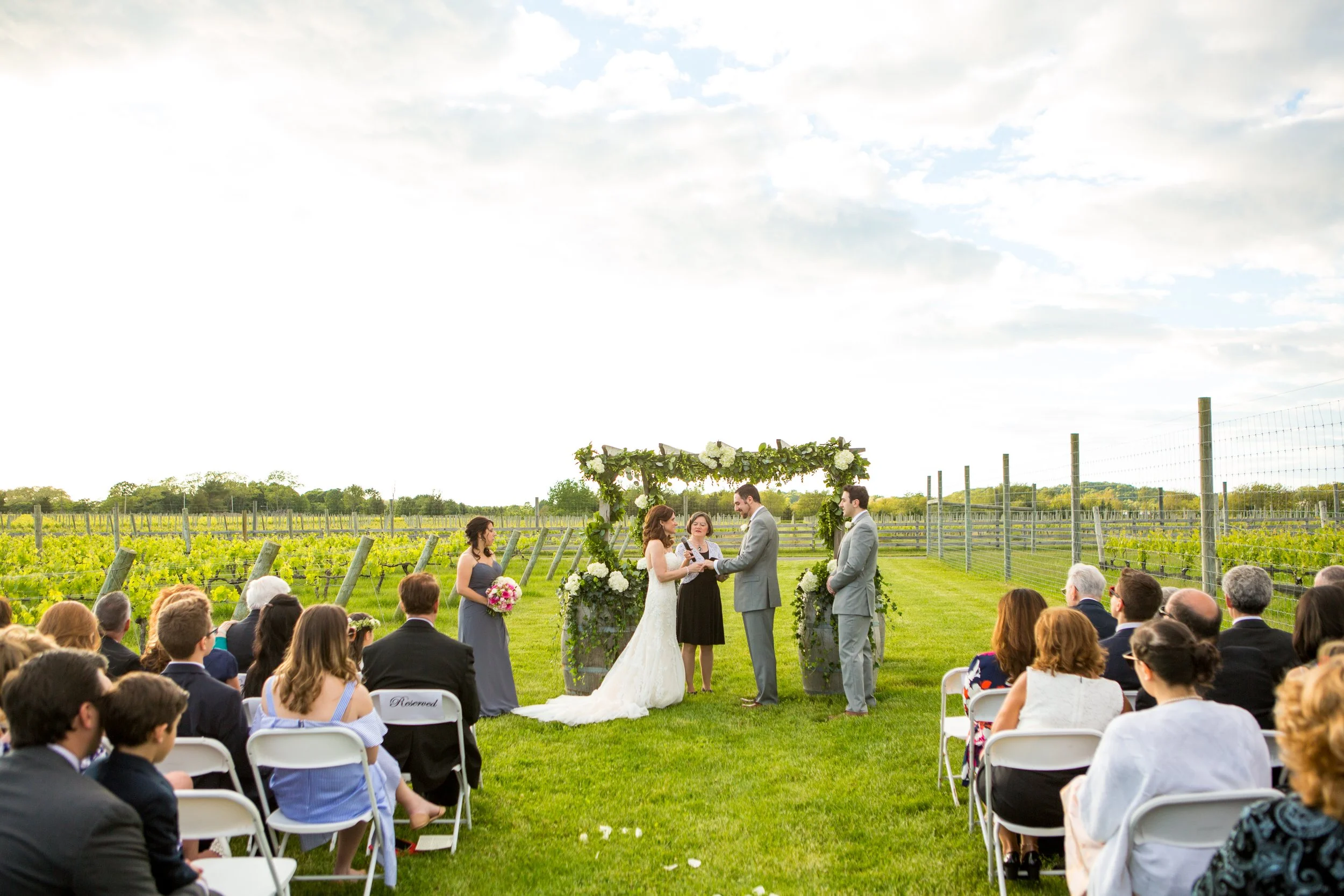 Loving couple getting married in a lush outdoor vineyard setting surrounded by friends and family.