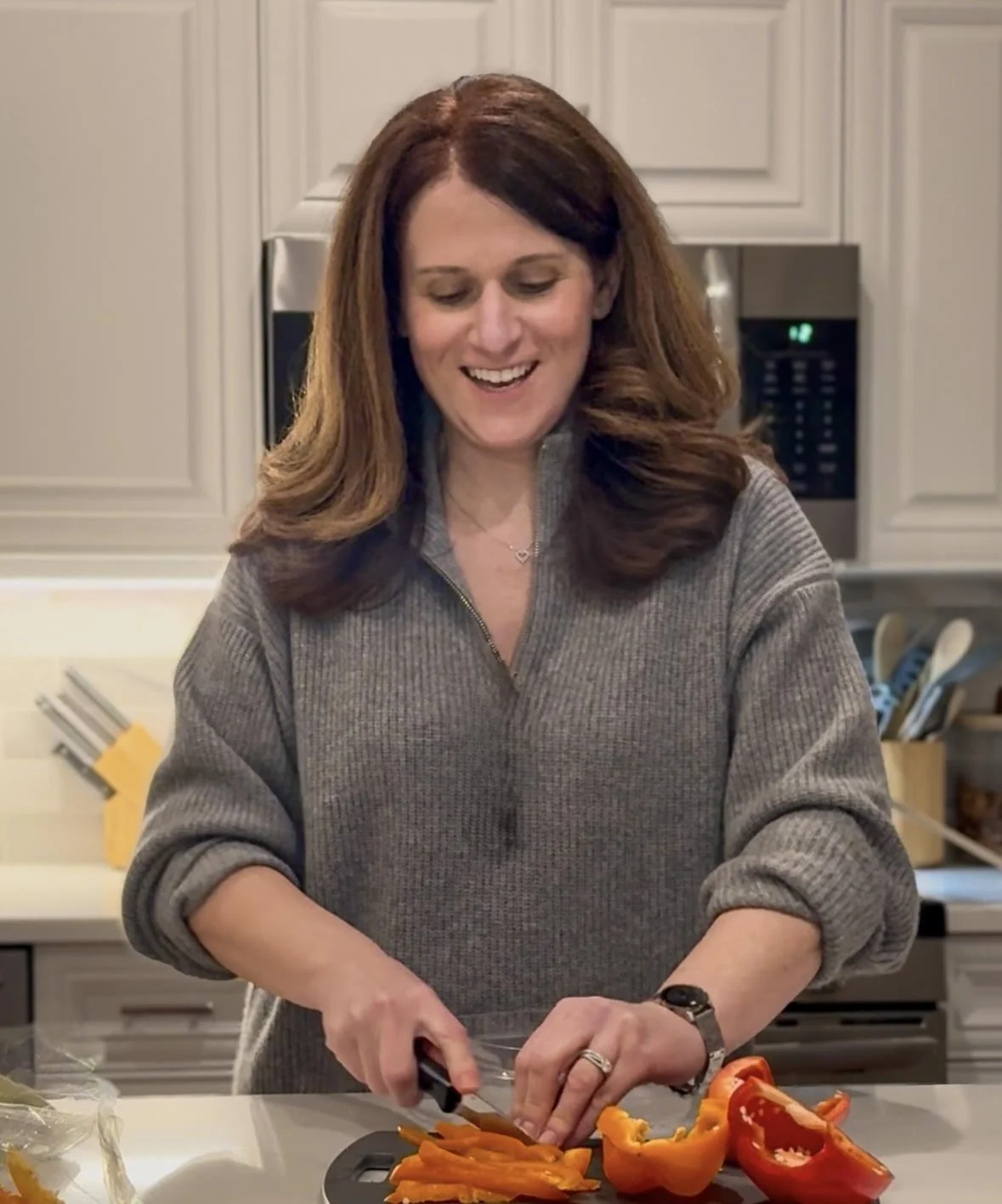 Woman chopping orange and red bell peppers in a kitchen.