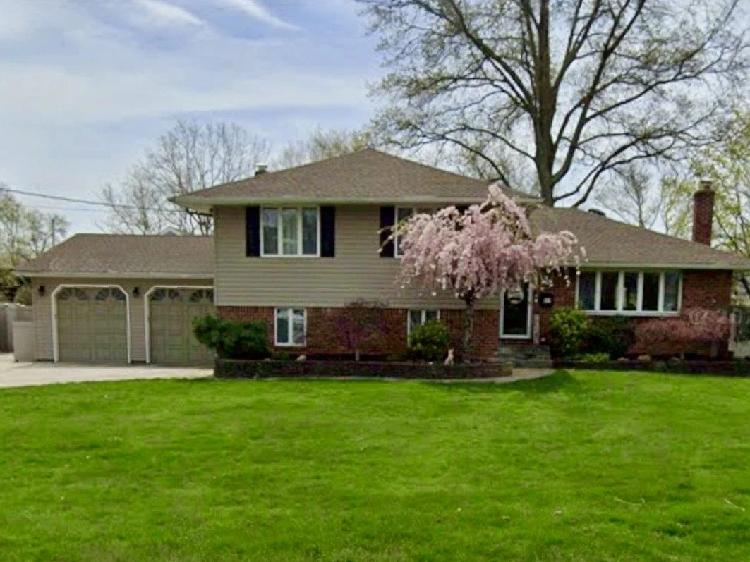 A warm and inviting house with brick and beige siding, surrounded by a green lawn and a blossoming pink tree in the front yard.