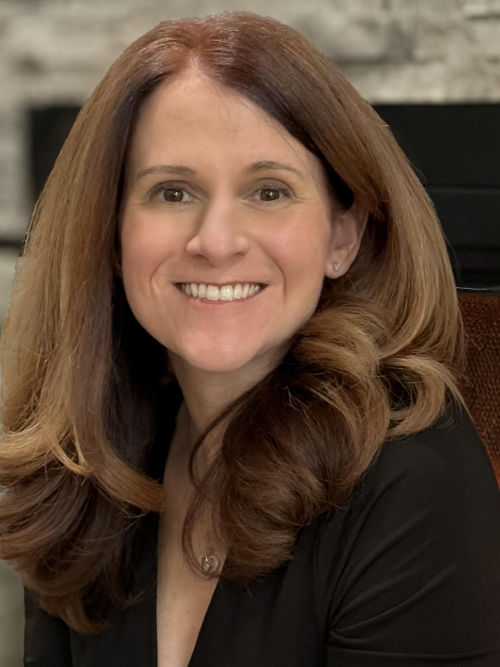 Close-up of a smiling woman with long red hair, wearing a black top, in an indoor setting. Expectant mother placing her baby for adoption.