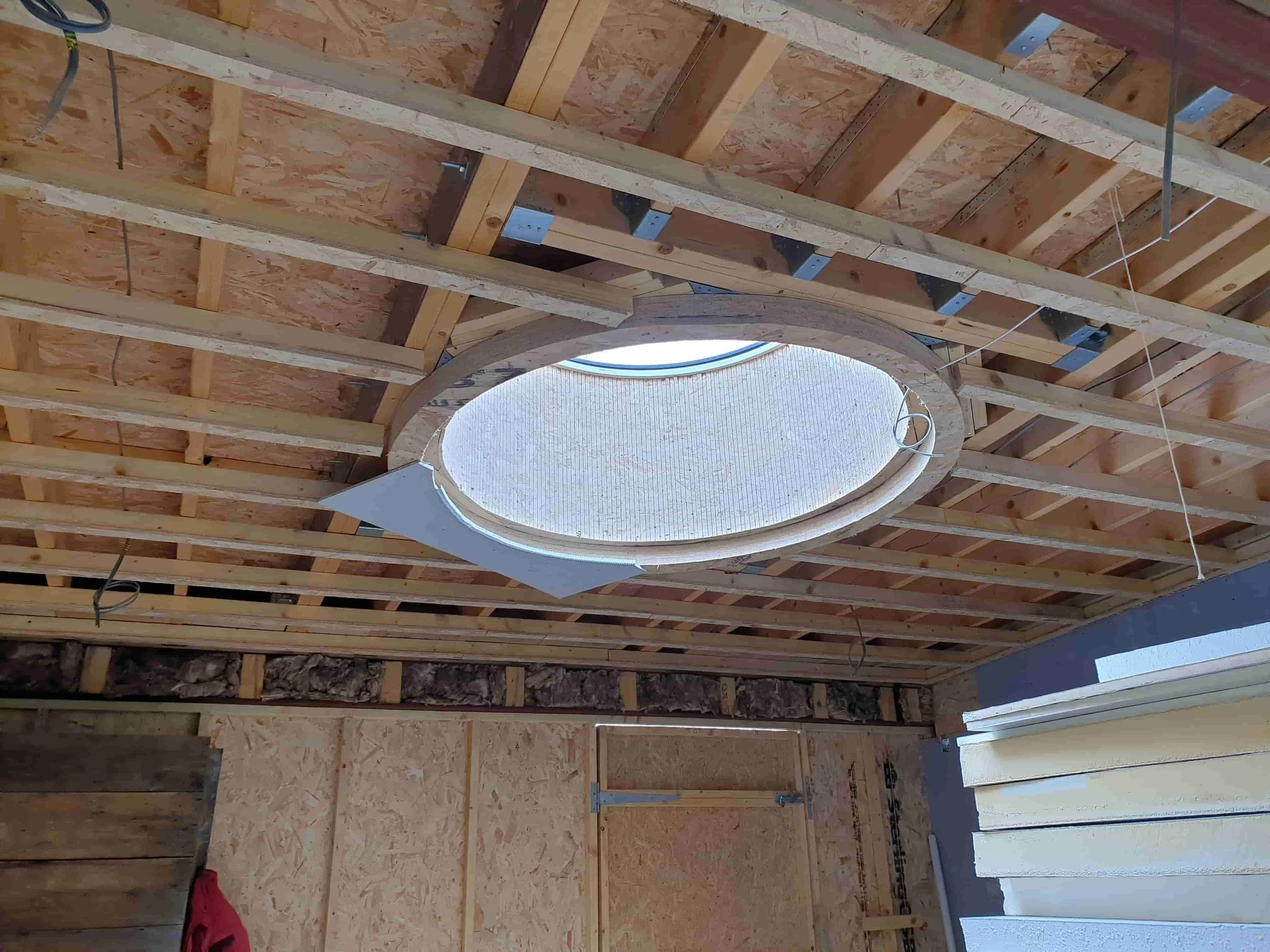 Construction site ceiling with exposed wooden framing and a round skylight in the center, surrounded by construction materials and insulation.