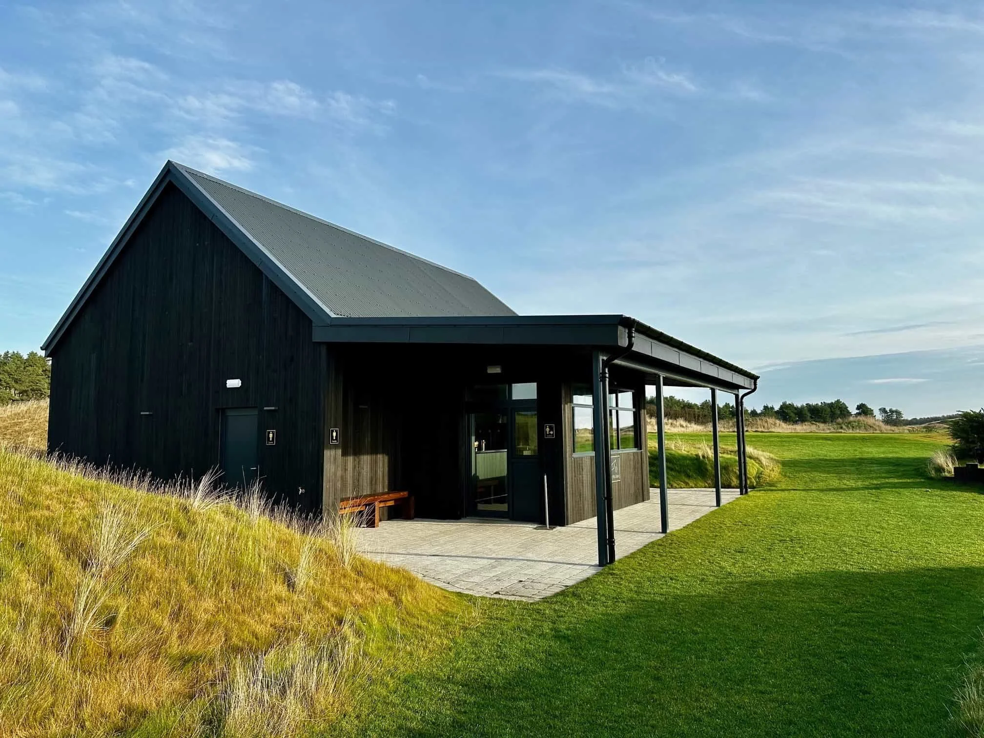 Modern black-clad golf clubhouse pavilion set within coastal landscape.