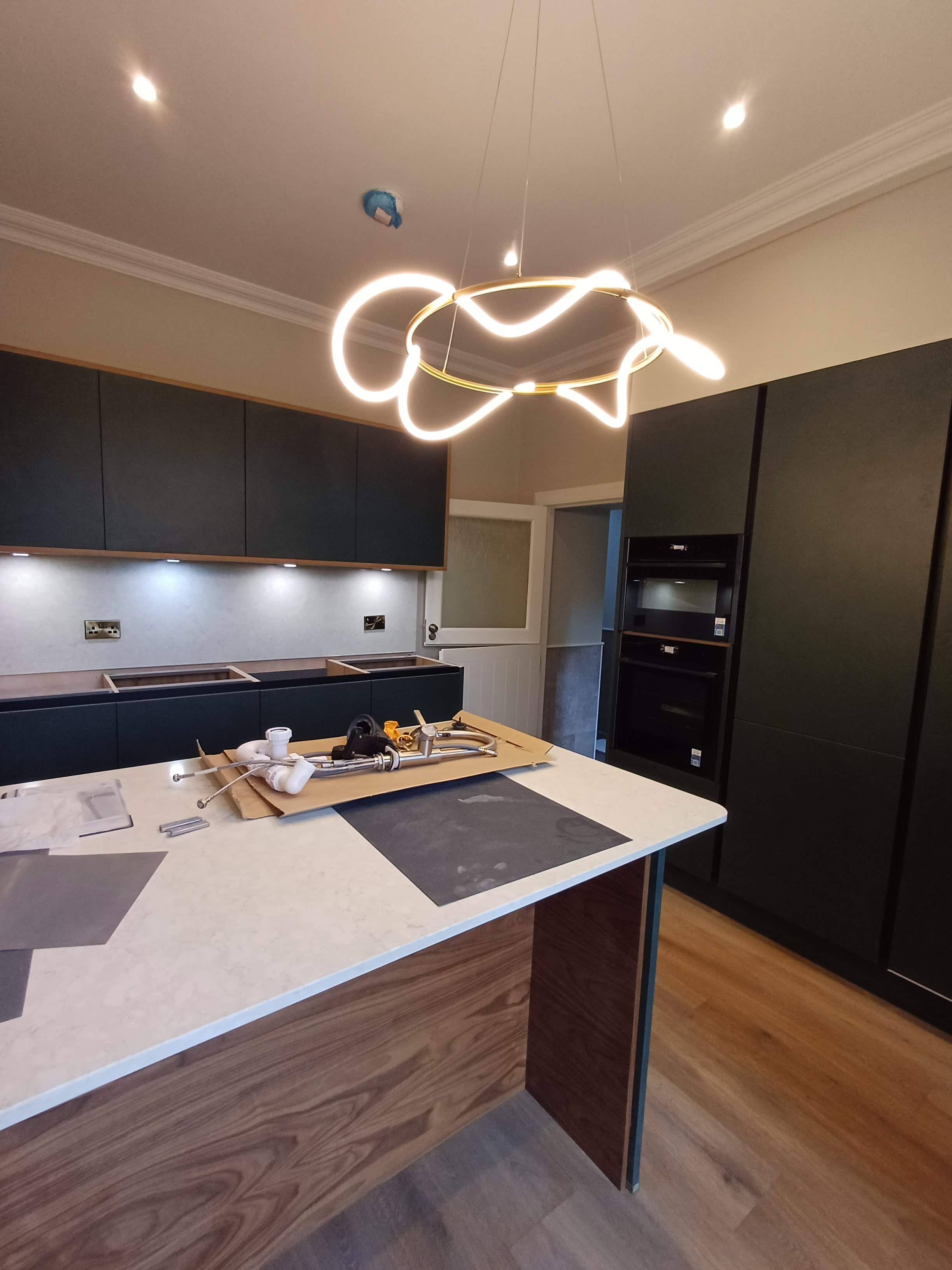 Modern kitchen under construction with black cabinets, a light-colored countertop, and a unique, illuminated ceiling light fixture.
