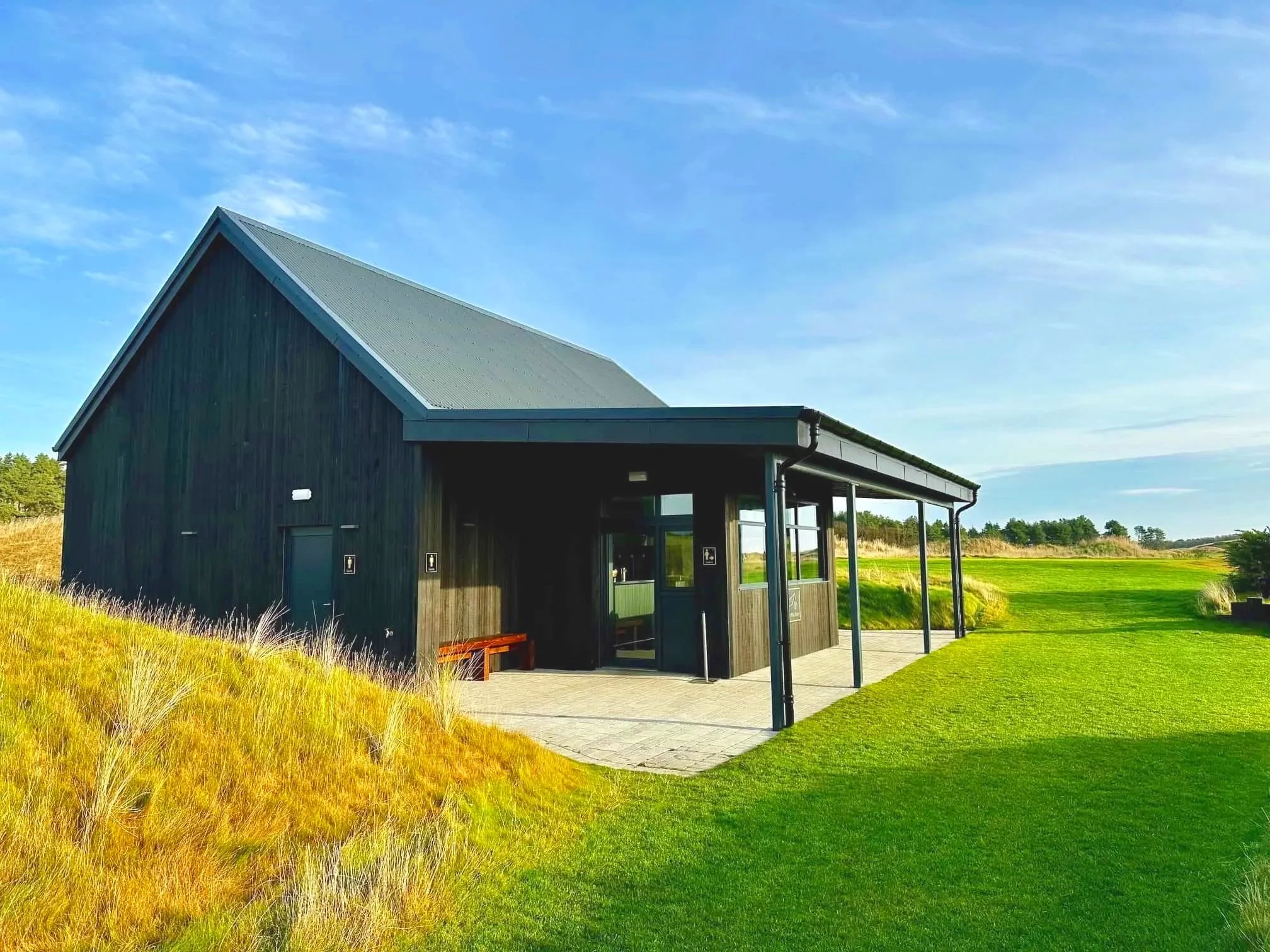 Modern black-clad golf clubhouse pavilion set within coastal landscape.