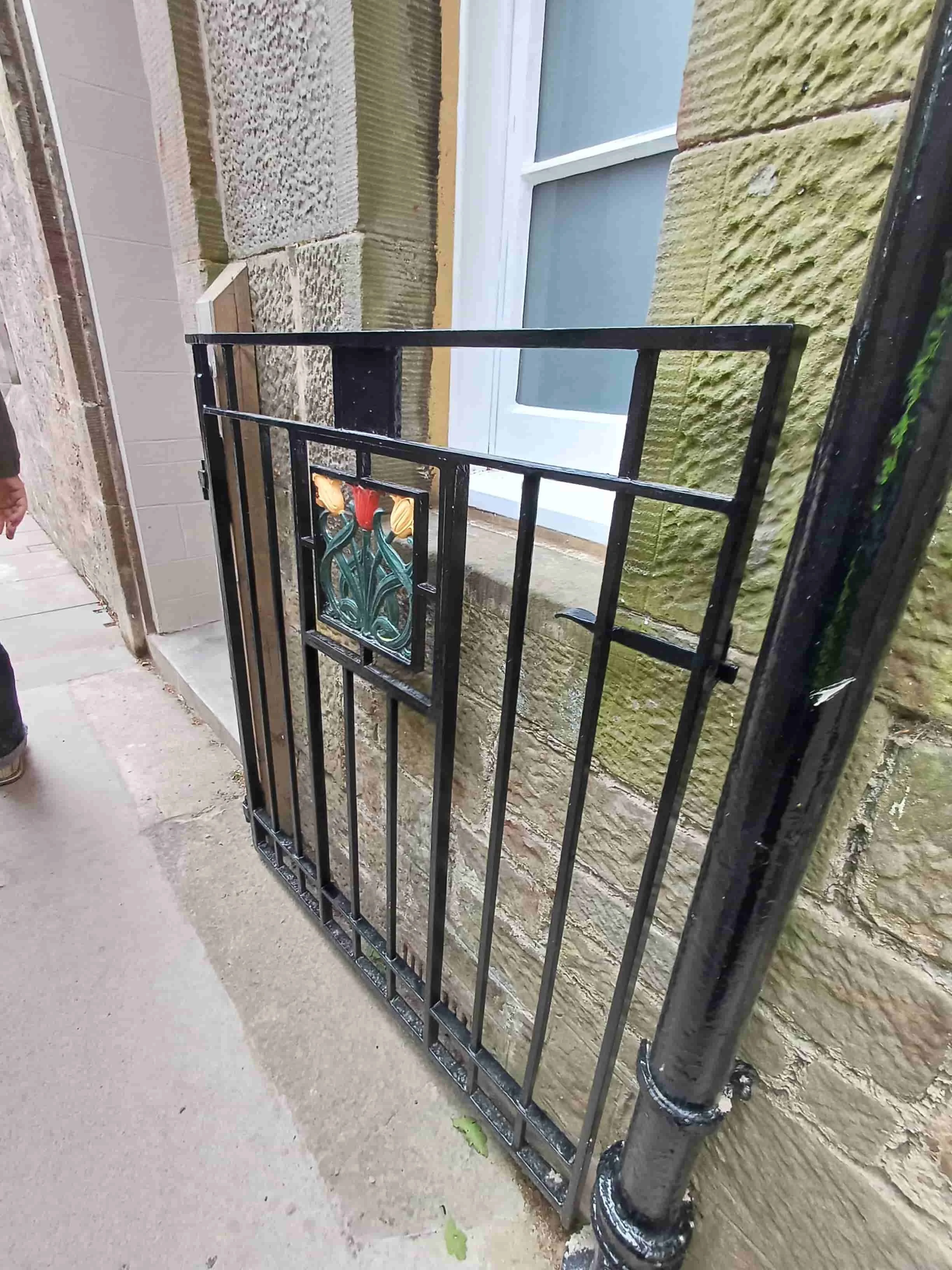 A decorative black metal gate with a floral design in front of a brick and stone building with a window.