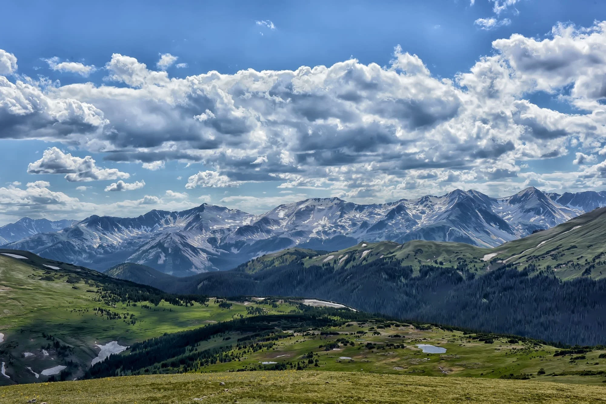 Scenic view of mountain range with snow-capped peaks, green valleys, and partly cloudy sky.
