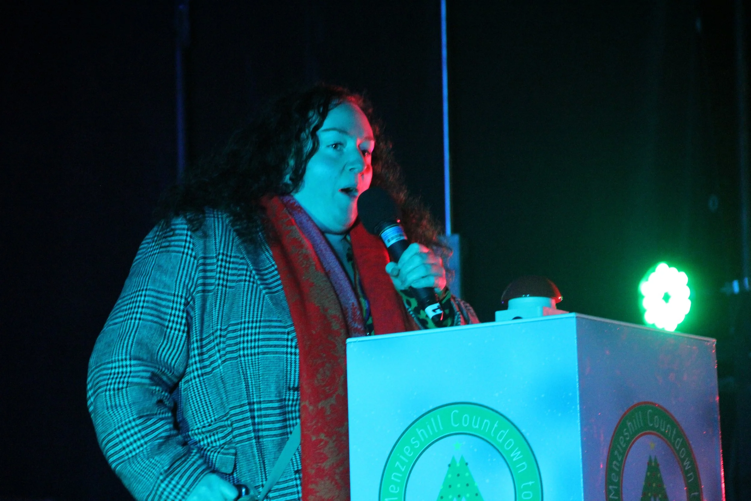 A woman with curly hair speaking into a microphone at a podium during an event.
