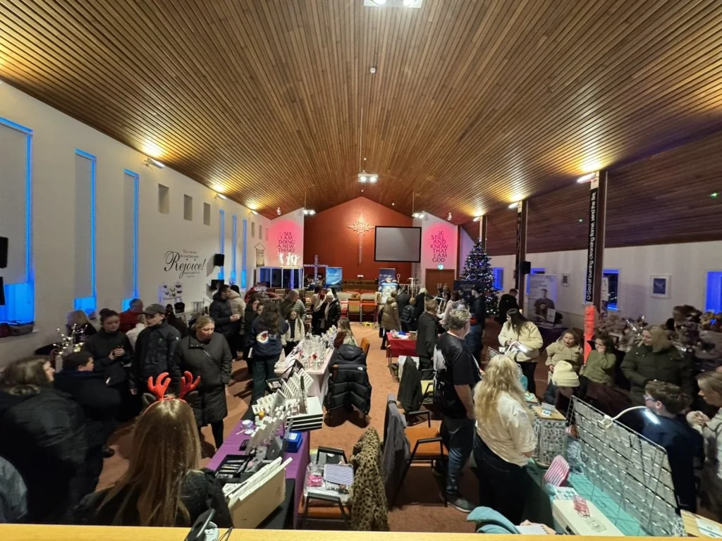 A Christmas-themed indoor market or event with many people browsing booths, decorated Christmas tree, and festive lighting.