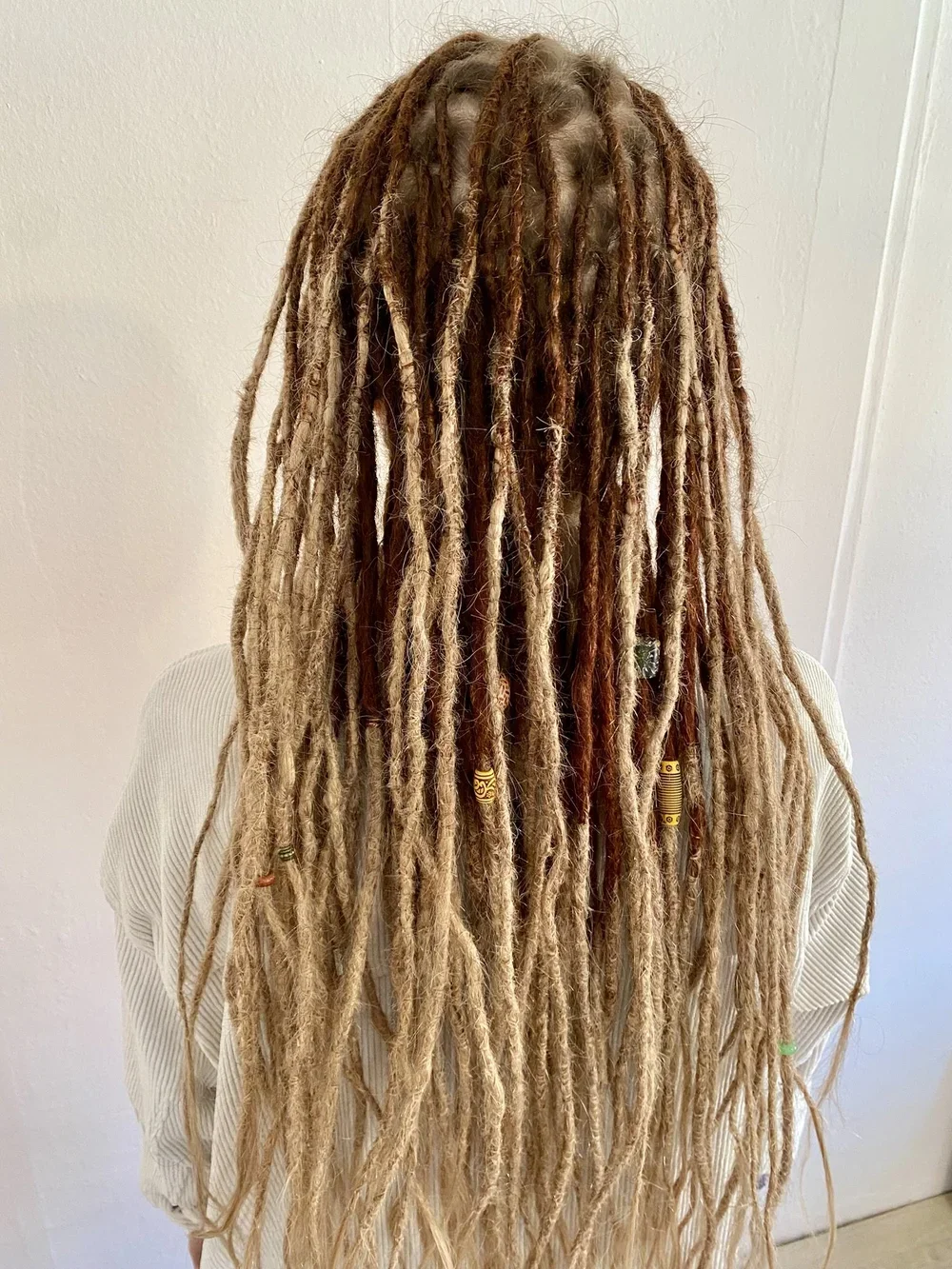 Person mit langen, geflochtenen Dreadlocks, die mit bunten Perlen und Dekorationen verziert sind, von hinten fotografiert.