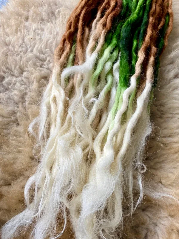 Wollfäden in den Farben braun, grün und weiß auf einem weichen, wollähnlichen Hintergrund.