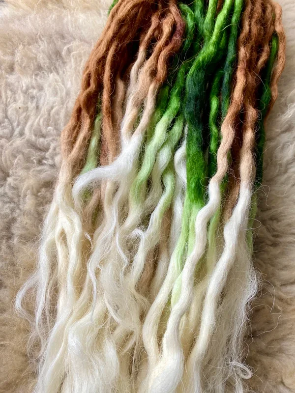 Bunte Dreadlocks mit braunen, grünen, weißen und limettengrünen Farben, liegen auf einem weichen Fell.