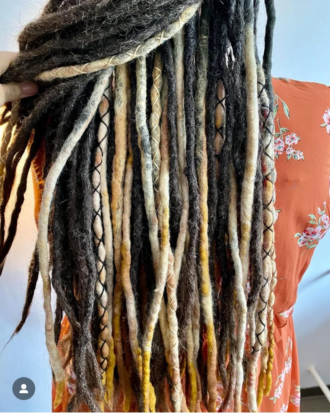 Hintergrund mit bunte Locken und Zöpfe von Dreadlocks, getragen von einer Person in einem orangefarbenen Kleid mit weißen Blumenmuster.