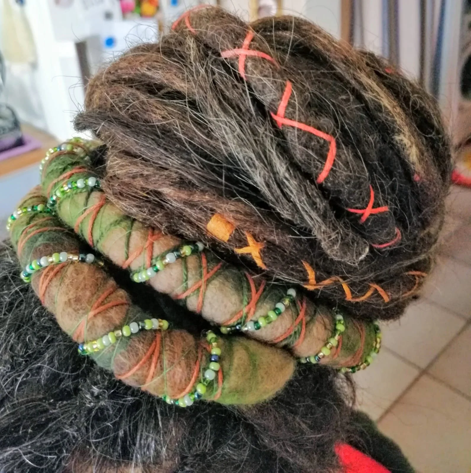 Dreadlocks mit bunten Perlen und bunten Bändern, Haare sind schwarz mit grauen Strähnen, die im Haar-Styling verwendet werden, in einem inneren Raum