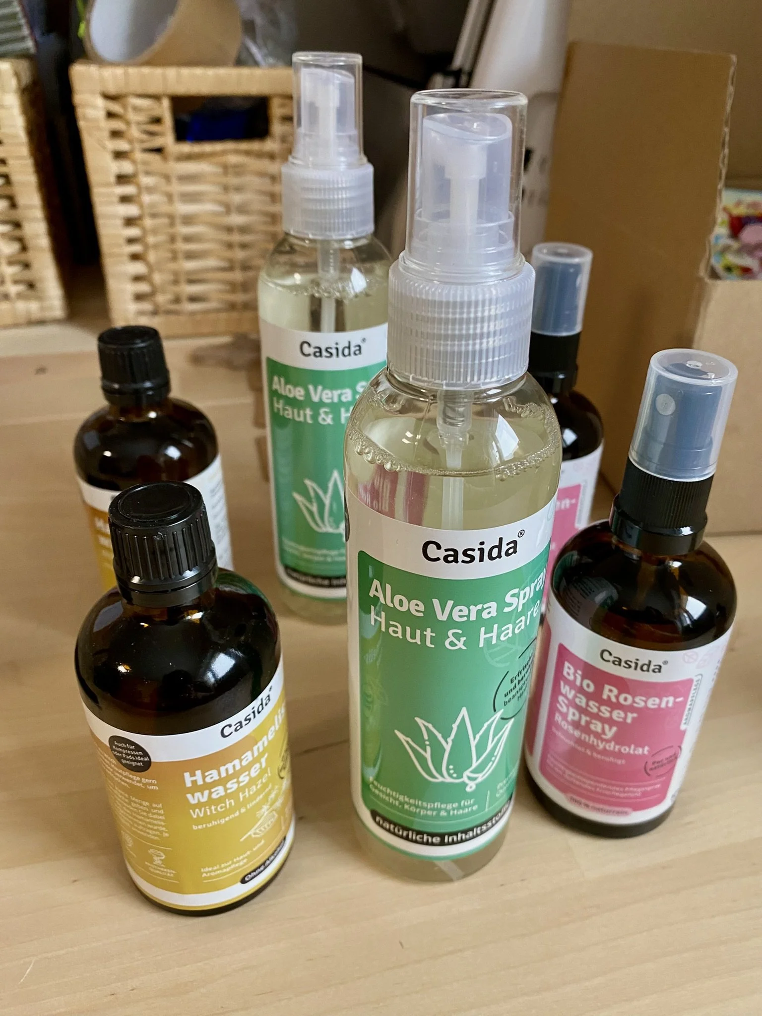Verschiedene Heilmittel und Hautpflegeprodukte in Flaschen auf einem Holztablett, darunter Aloe Vera Spray, Rosenspray und Hamameliswasser.