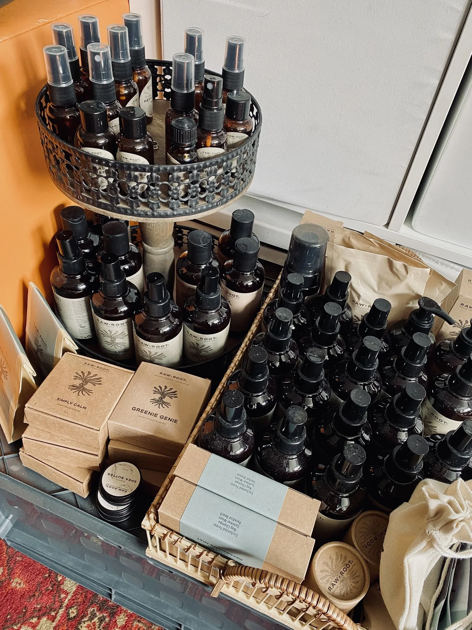 Verschiedene Hautpflege- und Wellnessprodukte in Flaschen, Tiegeln und Verpackungen auf einem Regal, darunter Sprühflaschen, Produkte in Pappschachteln und einer roten Teppichmatte.