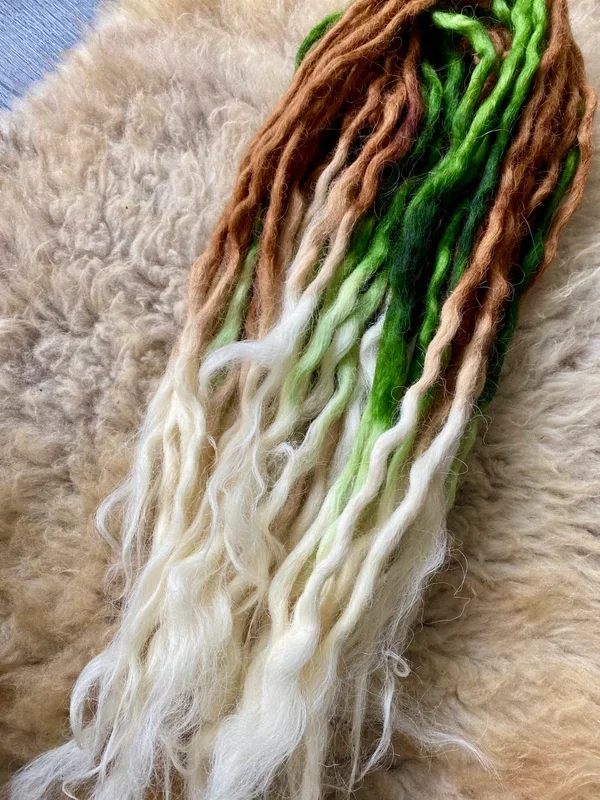 Färbende Lockenwolle in braun, grün, weiß, und blond, liegen auf einem Fell.