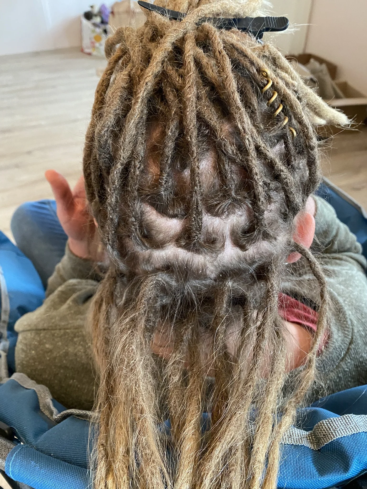Nahaufnahme eines Kopfes mit langen, dreadlocksartigen, blond-braunen Haaren, die mit kleinen Goldringen verziert sind.