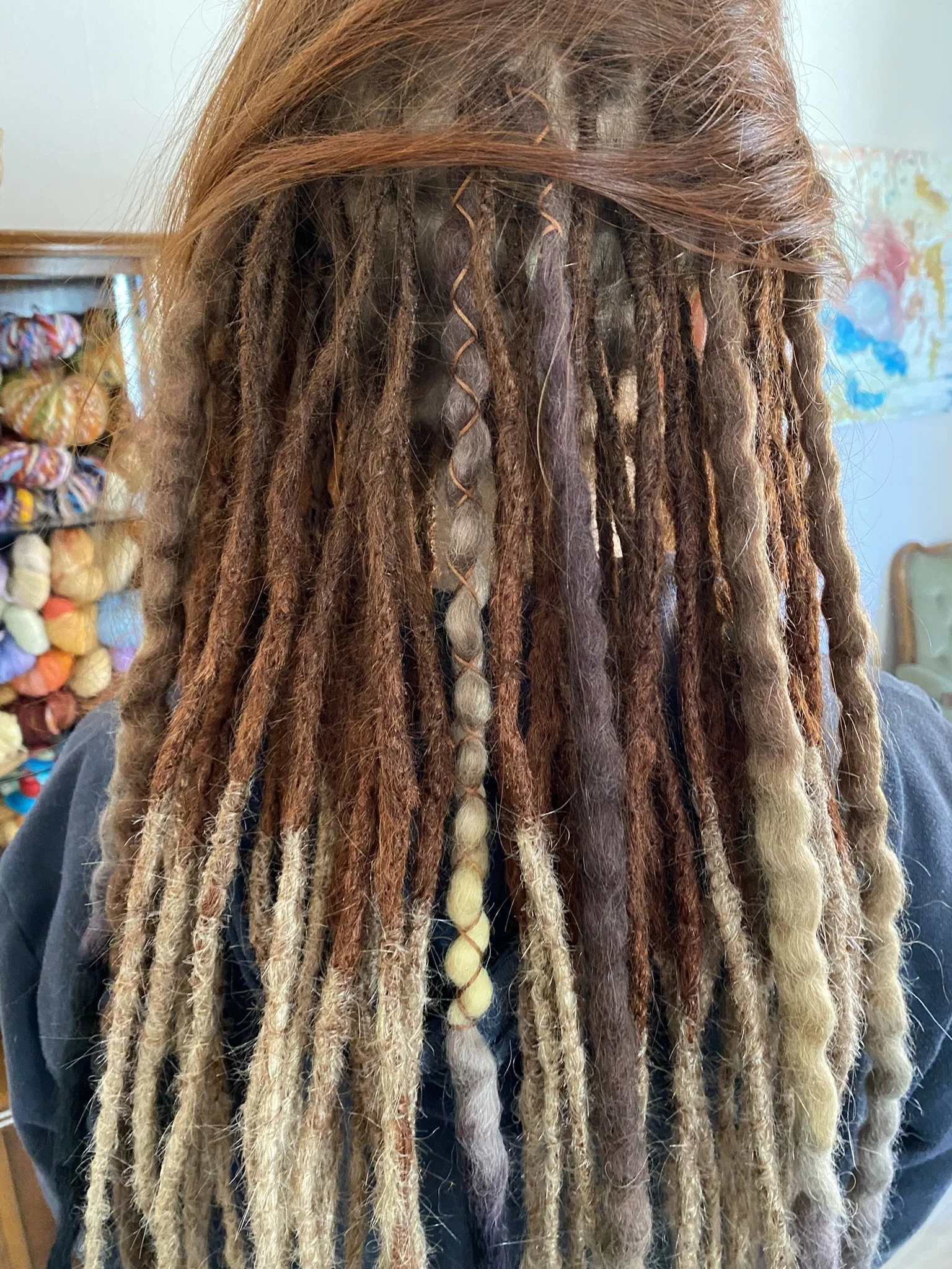 Frisur mit langen Dreadlocks in verschiedenen Brauntönen und einigen hellen, geflochtenen Elementen.