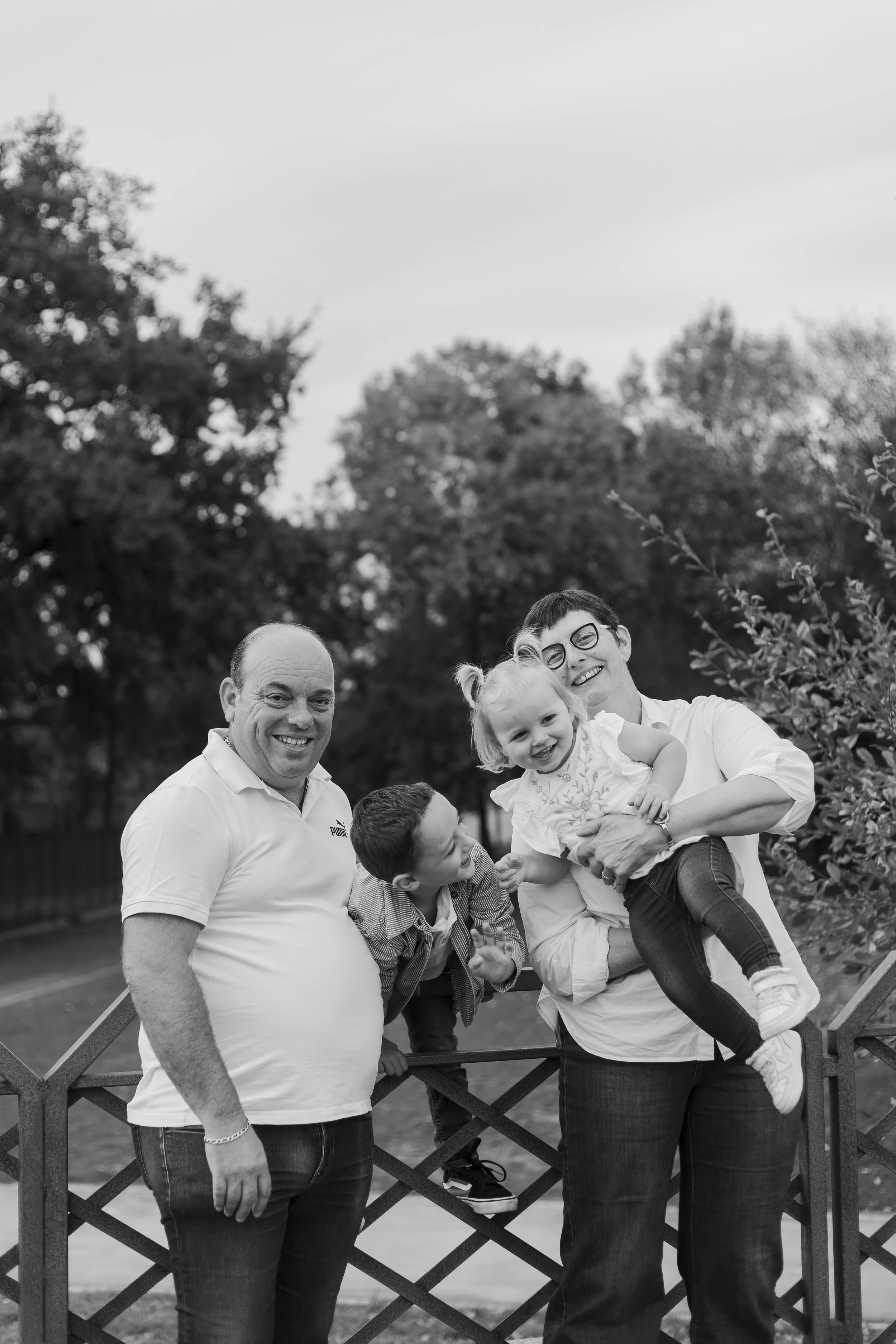 Une famille souriante avec deux adultes et deux enfants, posant dans un parc.