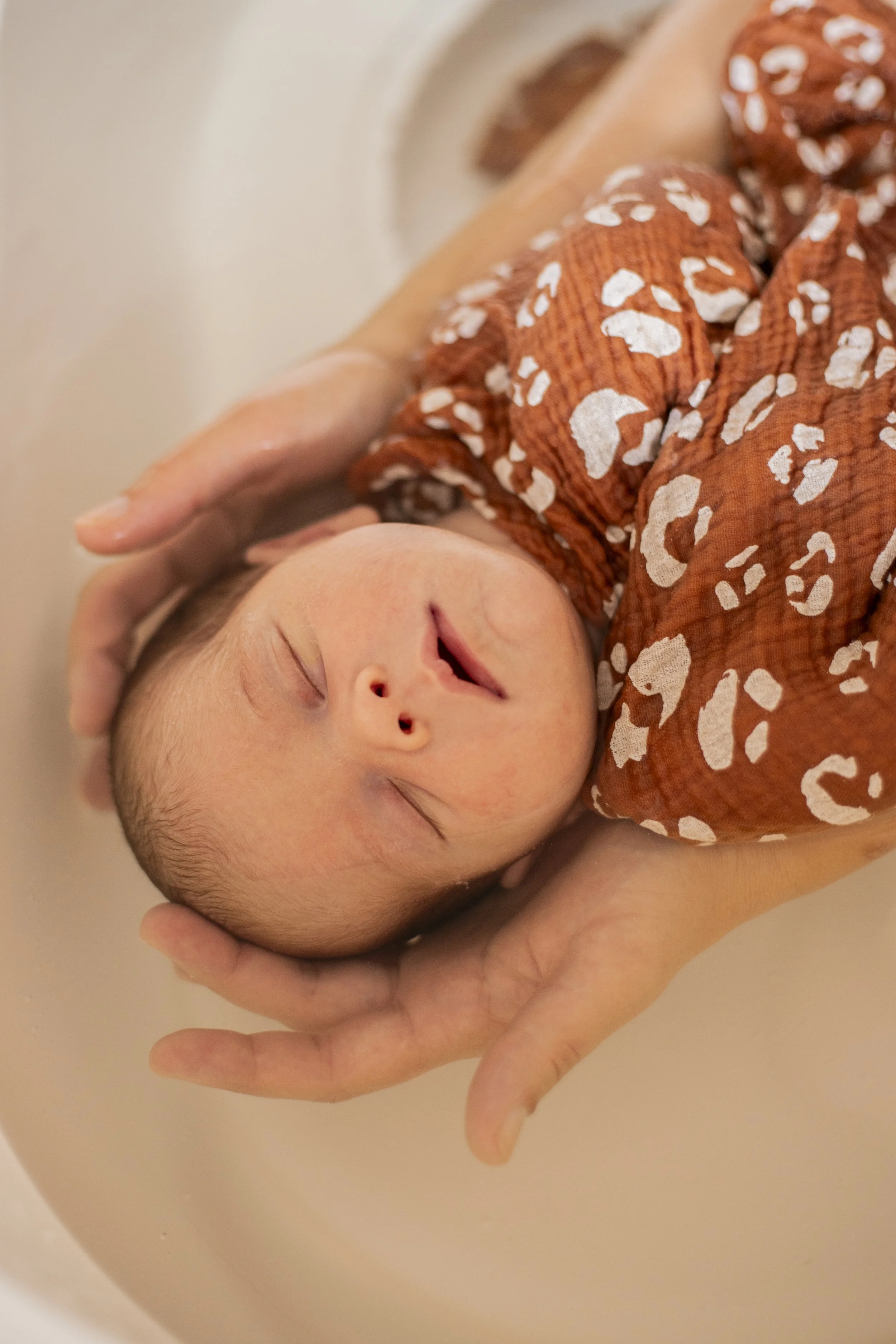 Un bébé dort paisiblement, tenu doucement par deux mains.