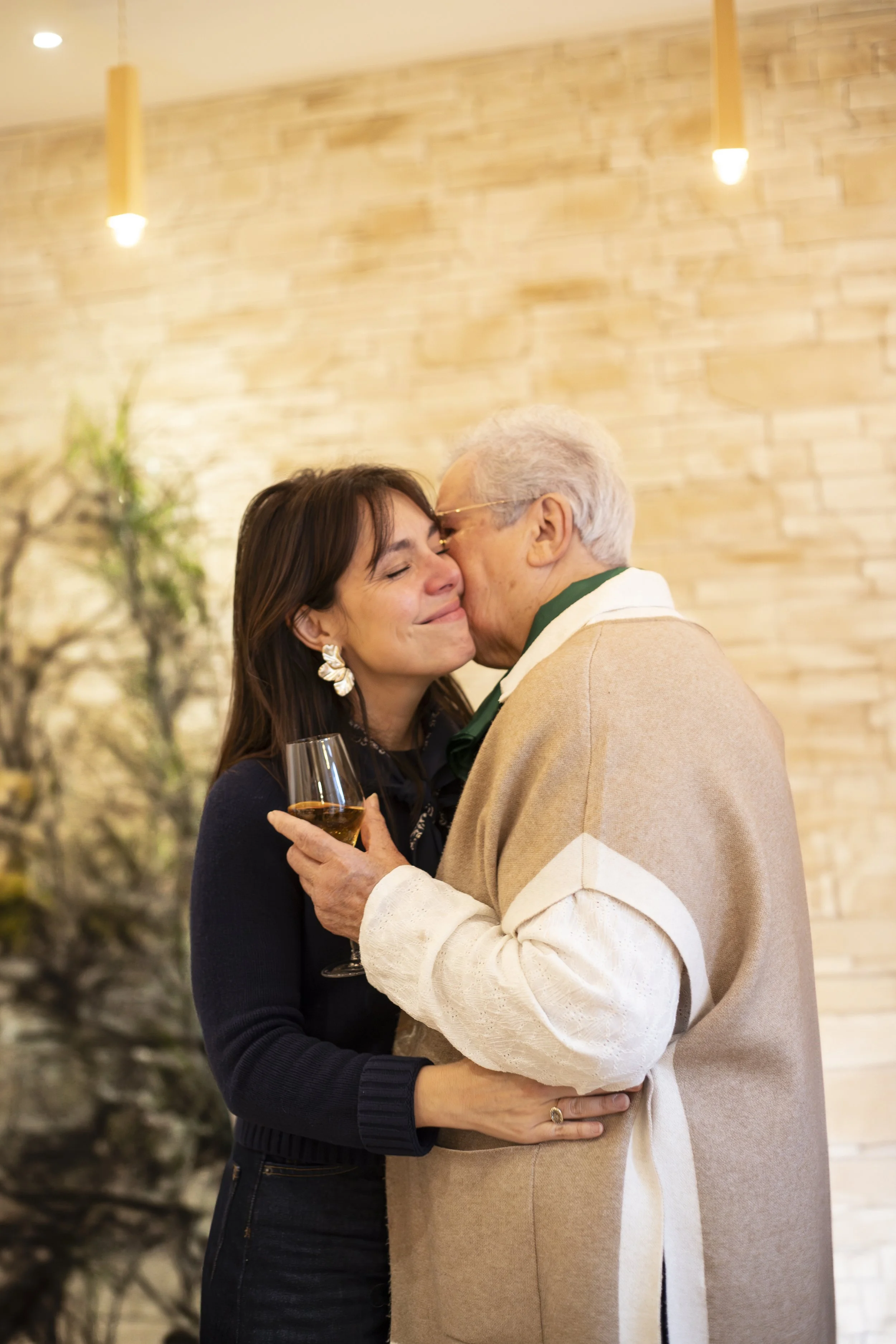 Deux personnes partagent un moment tendre en se donnant un baiser sur la joue tandis qu'une vitrine à l'arrière-plan évoque une ambiance chaleureuse.