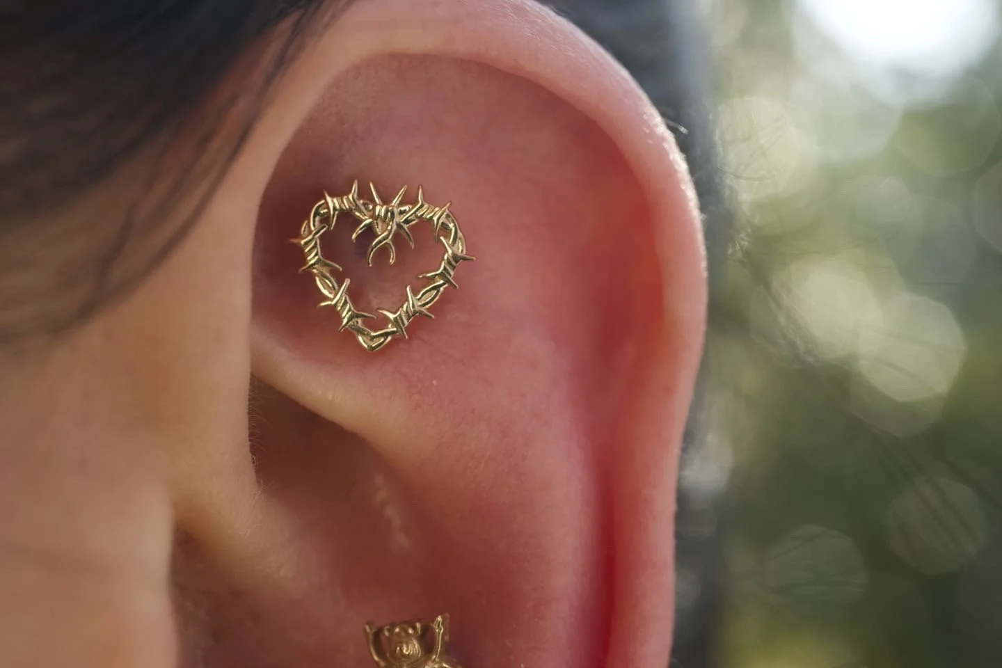 Close-up of a human ear with a gold heart-shaped cartilage ring made of barbed wire design.