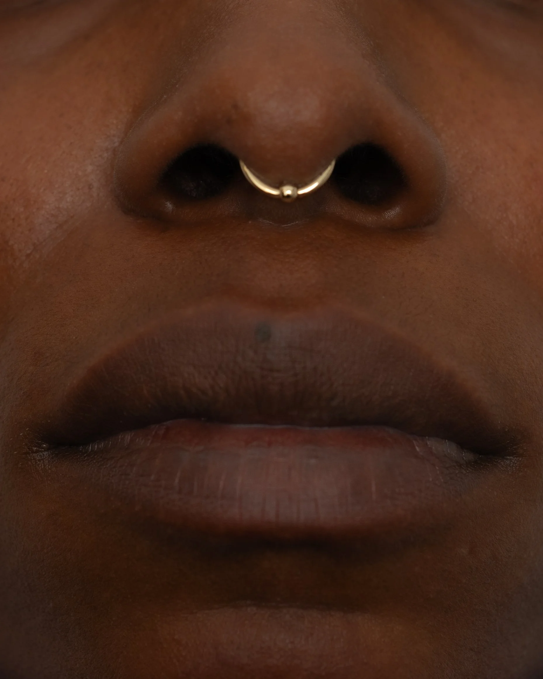 Close-up of a person's nose with a septum piercing and lips.