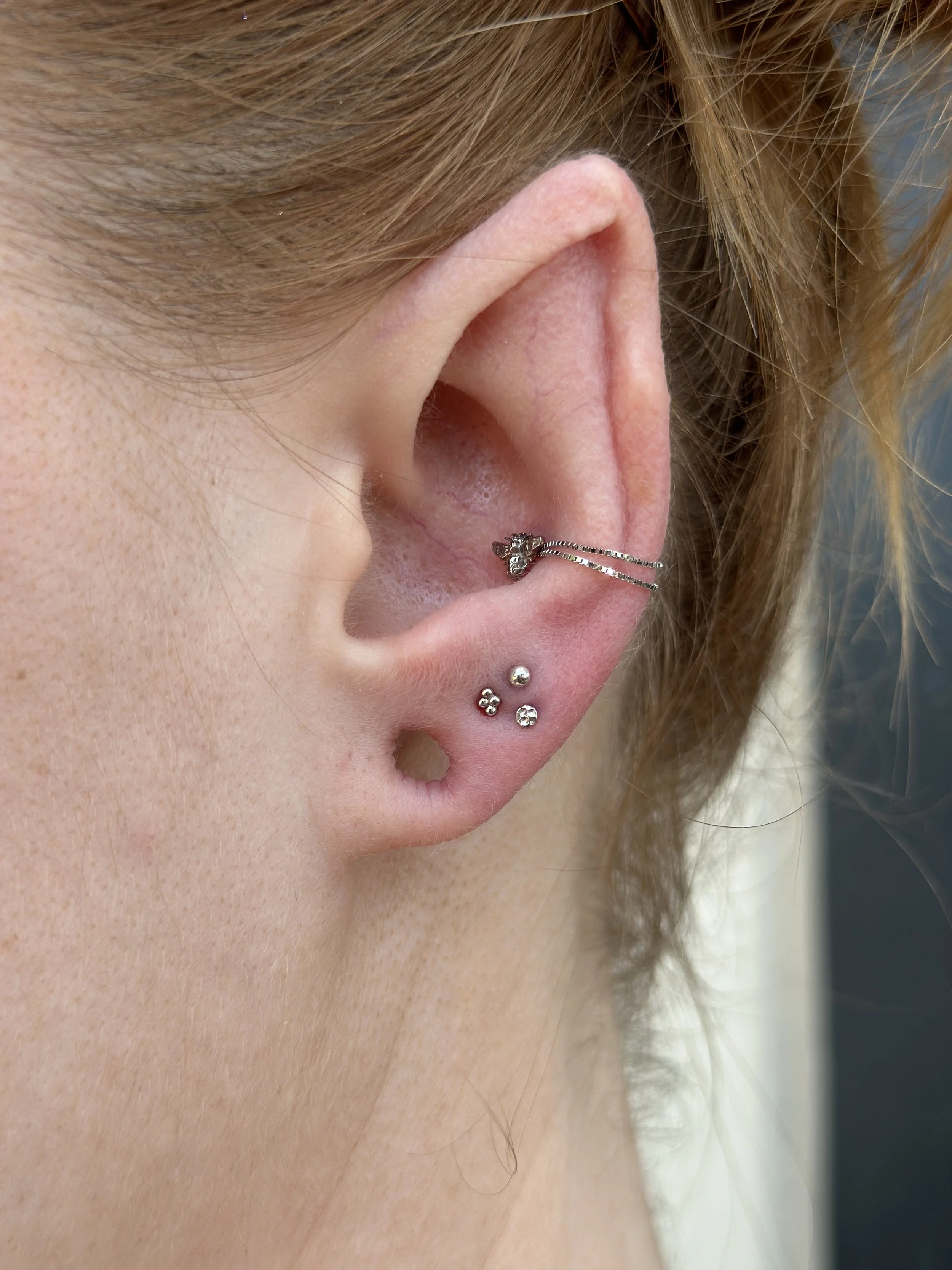 Close-up of a person's ear with multiple earrings, including a ear cuff with a small flower design, a stud with a clear gemstone, and several small diamond-shaped studs.