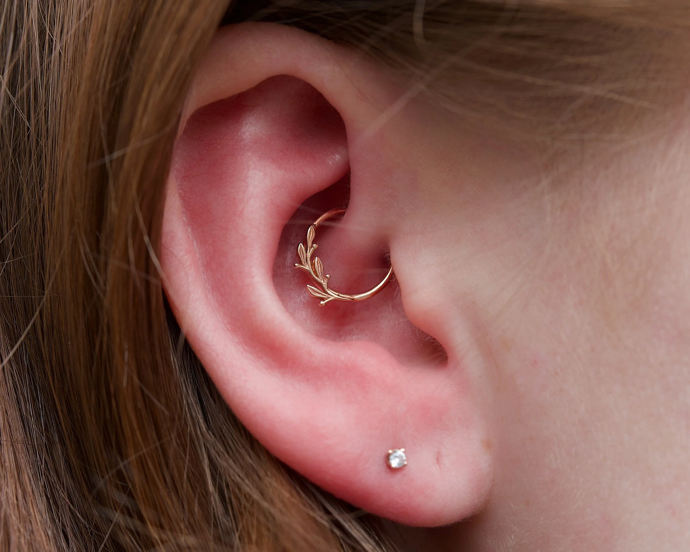Close-up of a woman's ear with a small diamond stud earring and a gold hoop earring with leaf design.