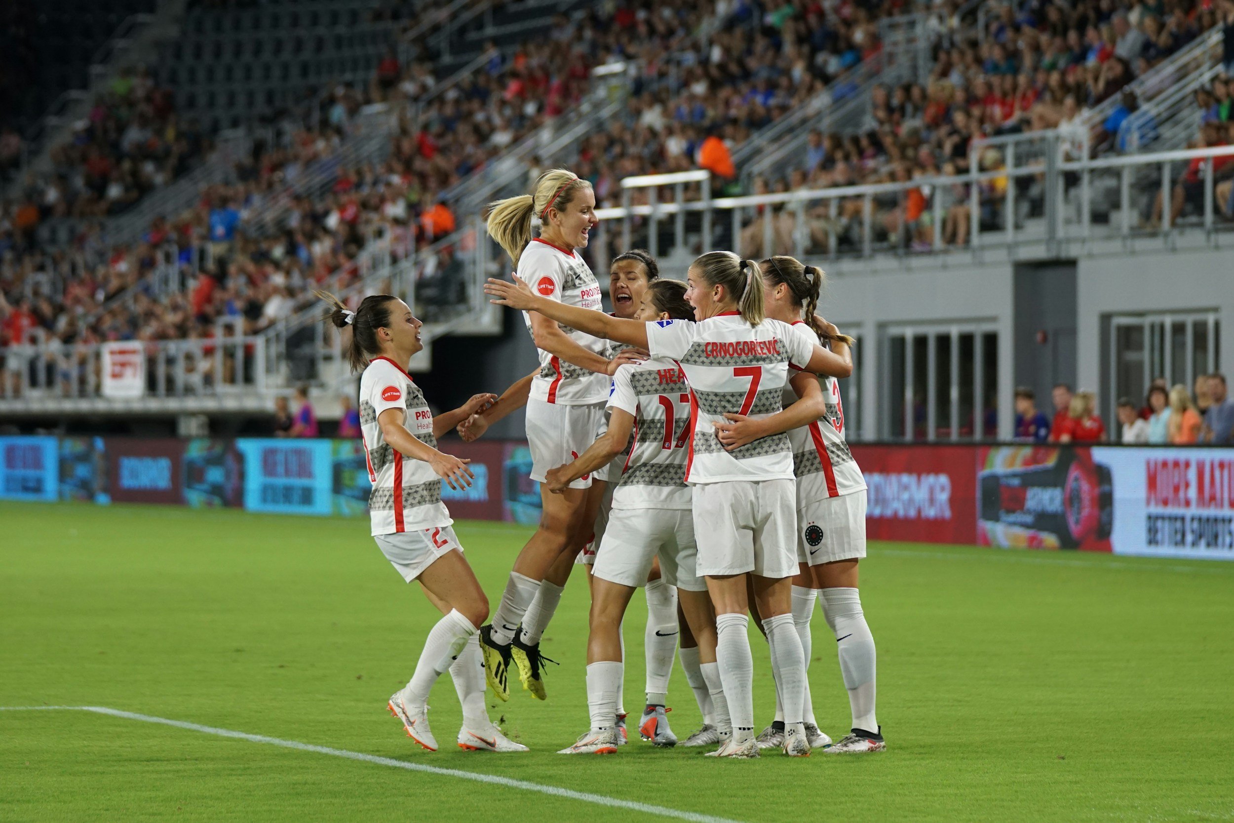 Soccer team in white uniforms celebrating on the field with spectators in the stands.