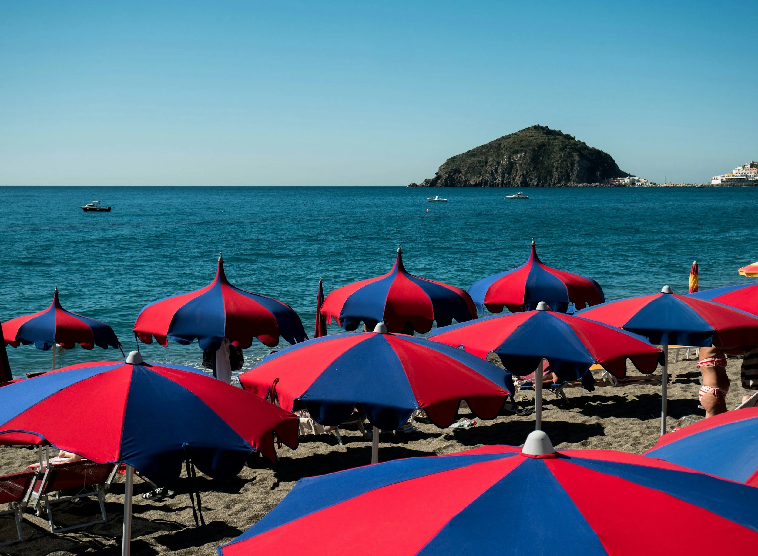 Beach scene with umbrellas on sand, ocean and a small island in the background.