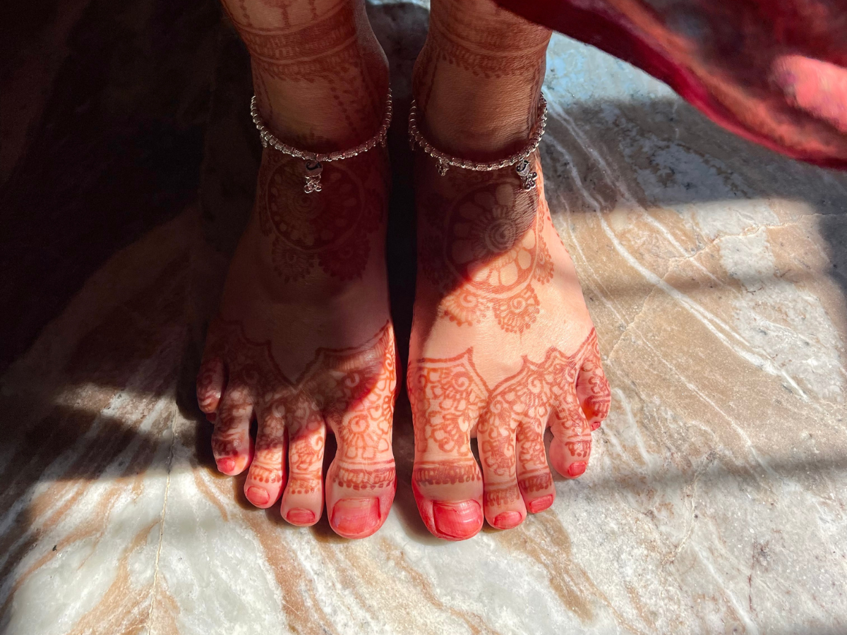 Feet with intricate henna designs, wearing silver anklets, standing on a marble floor.