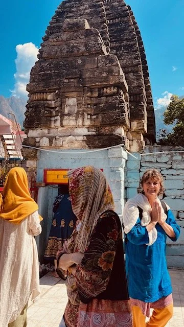 People praying in front of an ancient stone temple with a large carved head sculpture, under a blue sky.