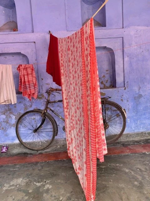 A bicycle leaning against a blue wall, with red and white patterned cloths hanging on a clothesline attached to the wall.