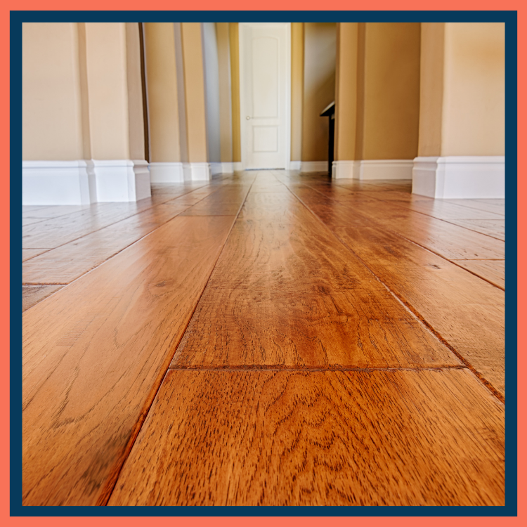 Low-angle view of hardwood floor boards in a hallway leading to a closed white door.